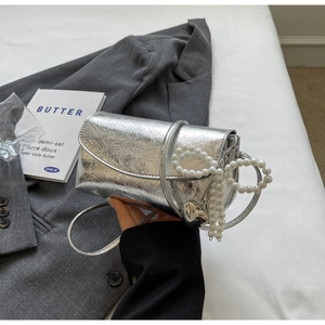 Detail of silver metallic handbag featuring a pearl bow handle and heart charm