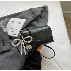 Detail of a black pleated crossbody bag with a pearl bow and silver heart pendant detail