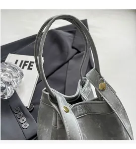 Détail du sac seau métallisé argenté avec garnitures dorées sur costume gris
