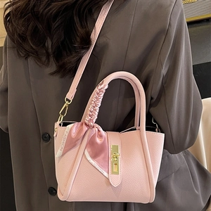 Pink lychee leather bucket bag with silk scarf handle and gold twist lock in crossbody view