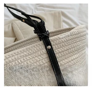 Detail of cream woven handbag showing black leather strap and silver metal rivets