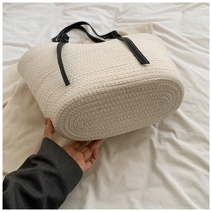 Detail of white woven tote bag featuring black leather handles and textured knit fabric
