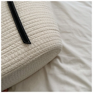 Close-up of cream woven beach bag featuring black leather strap with white stitching