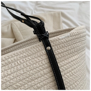 Close-up of woven tote bag featuring black leather handles and silver rivet details