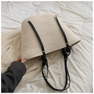 Detailed texture of cream woven tote bag with slim black leather straps on soft fabric