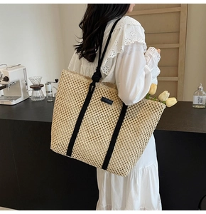 Gros plan d'un sac cabas en paille tissée ajourée avec anses noires et détail écusson