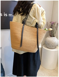 Detail of woven straw tote bag featuring black leather straps and white stitching contrast