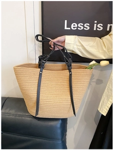 Detail of hand-held woven straw tote bag with black leather handles and contrast stitching