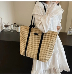 Vue latérale d'un sac cabas en paille tissée avec anses noires porté par un mannequin