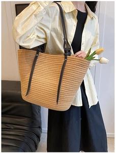 Woman wearing a large straw tote bag with black leather straps and white stitching
