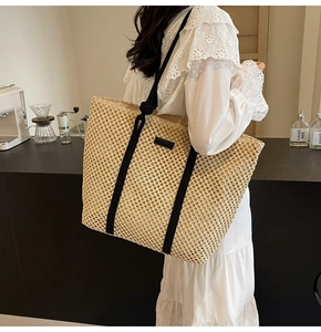 Détail d'un sac cabas en paille tissée beige avec des anses en toile noire sur modèle