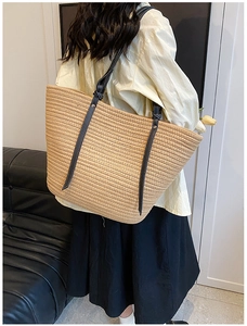 Detail of woven straw tote bag with black leather straps and white stitching accents