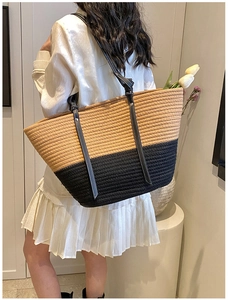 Detail of woven straw tote bag featuring contrast stitching on black leather shoulder straps