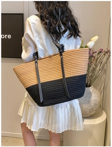 Close-up of a woven tote bag with black leather straps and white stitching on the handle