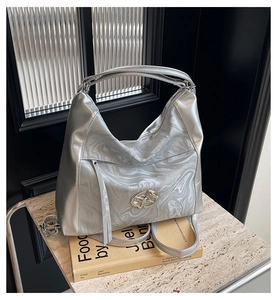 Dettaglio borsa hobo argento con motivo marmoreo e logo metallico su base marmo