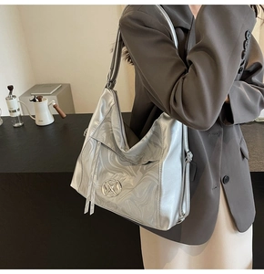 Dettaglio di borsa tote argento con trama metallica e logo circolare su tracolla larga