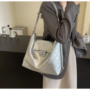 Close-up of a silver quilted tote bag featuring a metallic turn-lock and leather shoulder strap