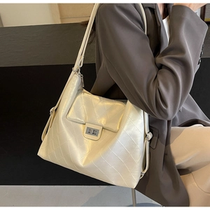Close-up of quilted cream tote bag with metal twist lock worn by a model in a suit