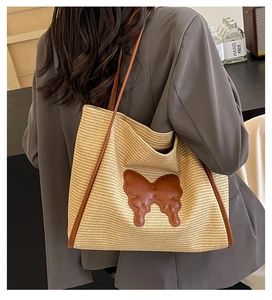 Detail of woven straw tote bag featuring brown leather butterfly applique and long shoulder strap