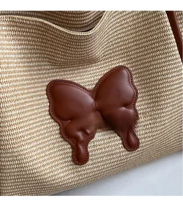 Close-up of woven straw handbag featuring a brown leather butterfly patch and metal zipper