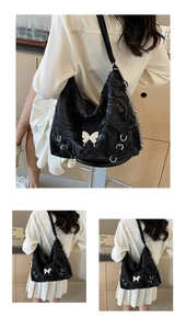 Detail of black fluid-textured tote bag featuring white butterfly badge and silver chains