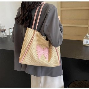 Detail of woven straw tote bag with pink butterfly applique and shoulder strap