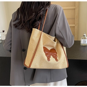 Detail of woven straw tote bag with brown leather butterfly patch on female model
