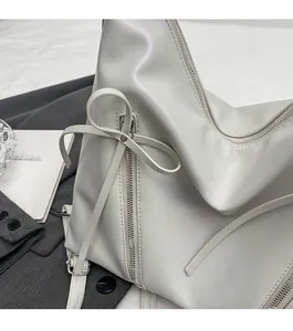Détail du sac cabas blanc avec nœud et fermeture éclair sur fond de costume gris