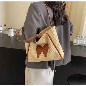 Detailed view of woven straw tote bag with brown leather butterfly patch on model