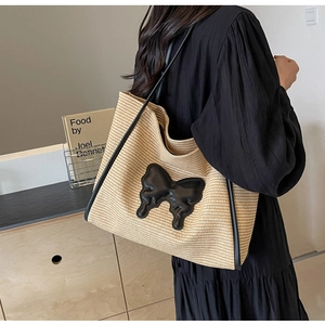 Detail of woven straw tote bag with black butterfly patch and leather shoulder strap