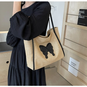 Detail of straw woven tote bag featuring black leather trim and butterfly patch