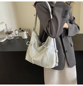 Détail du sac cabas en cuir crème avec nœud et zips porté par un mannequin décontracté