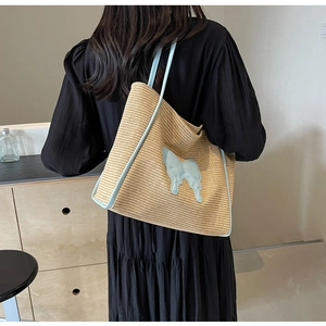Detail of woven straw tote bag with blue leather trim and a butterfly patch on model