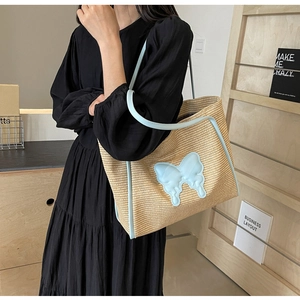 Detail of straw tote bag with blue butterfly patch and leather trim on black dress