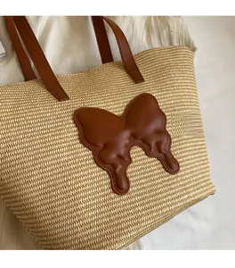 Close-up of beige woven straw tote with a large brown leather butterfly applique