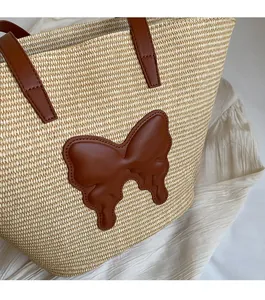Detail of white straw tote bag featuring a brown leather butterfly patch and long handles