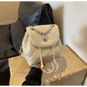 Close-up of beige quilted backpack with silver metal twist lock and chain strap detail