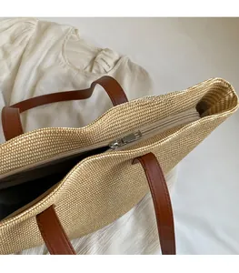 Detail of straw tote bag showing smooth metal zipper closure and brown leather handles