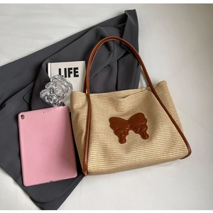 Straw tote bag with brown leather bow detail shown over a grey blazer background