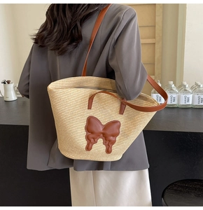 Detail of summer straw tote bag featuring brown leather butterfly patch and dual straps