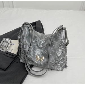 Detail of silver metallic tote bag with butterfly buckle on white bedding background