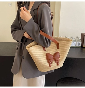 Straw tote bag detail with leather butterfly patch and dual-strap handles