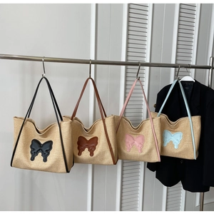 Detail of woven straw tote bags with butterfly patches in four colors on a metal stand