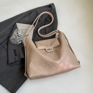 Beige quilted tote bag with metal twist lock and dual straps on grey blazer