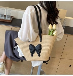 Detail of summer straw tote bag featuring 3D butterfly patch and black shoulder straps
