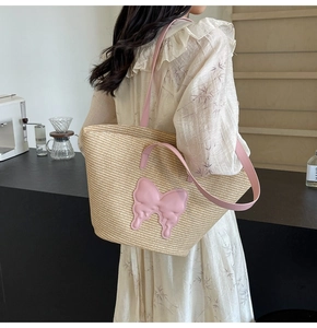 Close-up of woven straw tote bag featuring pink butterfly patch and matching leather straps