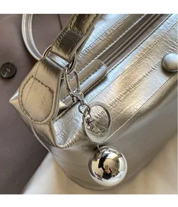 Detailed shot of silver textured shoulder bag with metallic spherical pendant and hardware