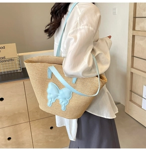 Detail view of woven tote bag showing blue faux leather handles and butterfly patch decoration