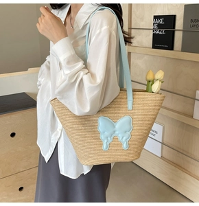 Detail of straw tote bag featuring 3D light blue leather butterfly and slim shoulder straps