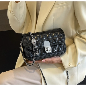 Detail of black quilted chain bag with silver lock and decorative metal ball charm